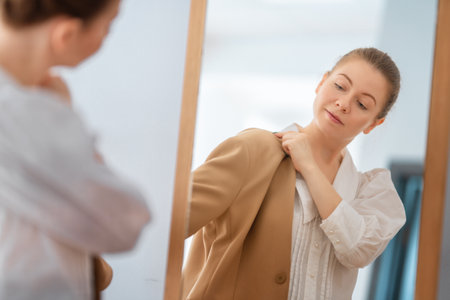 Self confident single woman looking at her reflection in mirror, putting on business clothes.の写真素材