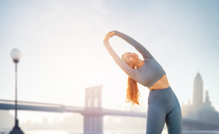 Young sportswoman is warming up, training or doing stretch exercise outdoors in summer morning.