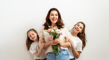 Happy women's day. Children are congratulating mom and giving her pink flowers. Mum and girls smiling on light grey background. Family holiday and togetherness.の写真素材
