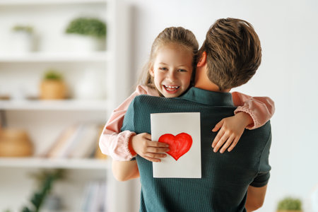 Child daughter is congratulating her father and giving him postcard. Dad and girl are smiling and hugging. Family holiday and togetherness.の写真素材