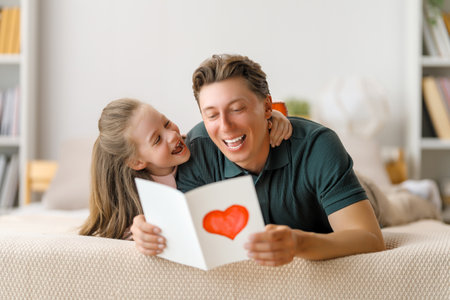 Child daughter is congratulating her father and giving him postcard. Dad and girl are smiling and hugging. Family holiday and togetherness.の写真素材