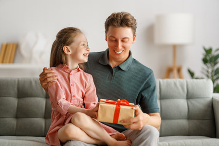 Happy father's day! Child daughter congratulating dad and giving him gift box. Daddy and girl smiling and hugging. Family holiday and togetherness.の写真素材