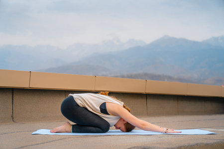 Young sportswoman is doing yoga exercise on rooftop of parking, garage in summer day morning.の写真素材