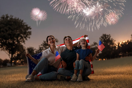 Patriotic holiday. Happy family, father, mother and daughter child girl with American flag looking at fireworks on city landscape background. USA celebrate 4th of July.の写真素材