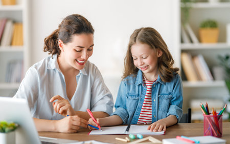 Happy child and adult are sitting at desk. Girl doing homework or online education.の写真素材