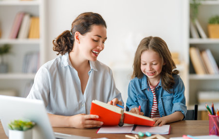 Happy child and adult are sitting at desk. Girl doing homework or online education.の写真素材