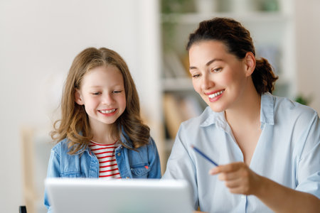Happy child and adult are sitting at desk. Girl doing homework or online education.の写真素材
