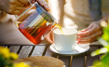 Pouring black tea into glass cup on wooden table in sunny morning.の写真素材