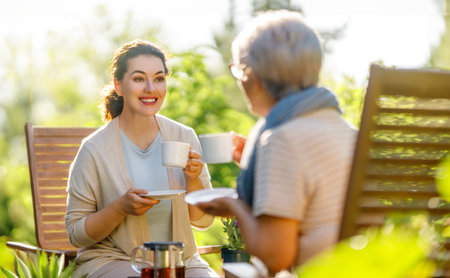 Happy young woman and her mother drinking tea in summer morning. Family sitting in the garden with cups and enjoying the conversation.の写真素材