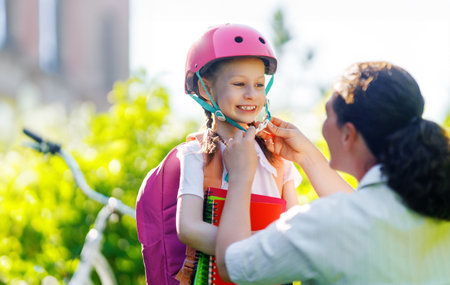 Girl  in safety helmet with bike and backpack. Happy child with mother. Safe way for kids to schoolの写真素材