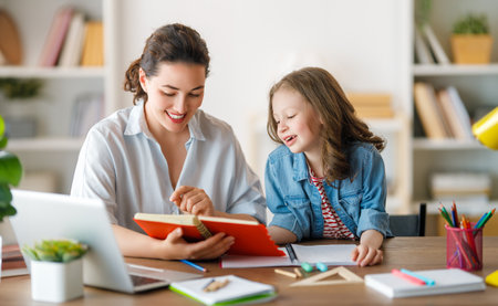 Happy child and adult are sitting at desk. Girl doing homework or online education.の写真素材