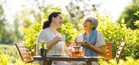 Happy young woman and her mother drinking tea in summer morning. Family sitting in the garden with cups and enjoying the conversation.の写真素材