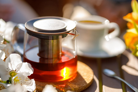 White cup and glass teapot with fresh tea on wooden table in summer light.の写真素材