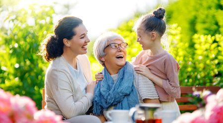 Happy little girl, her mother and grandmother drinking tea in summer morning. Family sitting in the garden with cups and enjoying the conversation.の写真素材