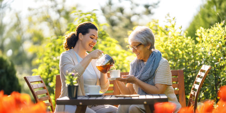 Happy young woman and her mother drinking tea in summer morning. Family sitting in the garden with cups and enjoying the conversation.の写真素材