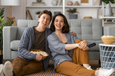 Happy family with popcorn sitting on sofa at home. Couple spending time together.の写真素材