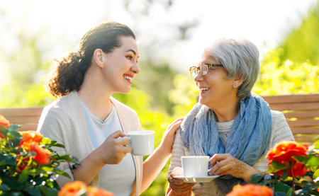 Happy young woman and her mother drinking tea in summer morning. Family sitting in the garden with cups and enjoying the conversation.の写真素材