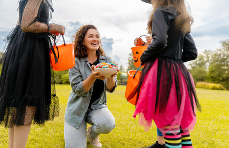 Happy people celebrating Halloween. Adult is treating with sweets children outdoors.の写真素材