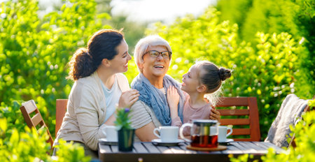 Happy little girl, her mother and grandmother drinking tea in summer morning. Family sitting in the garden with cups and enjoying the conversation.の写真素材