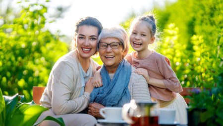 Happy little girl, her mother and grandmother drinking tea in summer morning. Family sitting in the garden with cups and enjoying the conversation.の写真素材