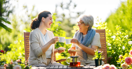 Happy young woman and her mother drinking tea in summer morning. Family sitting in the garden with cups and enjoying the conversation.の写真素材
