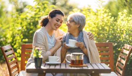 Happy young woman and her mother drinking tea in summer morning. Family sitting in the garden with cups and enjoying the conversation.の写真素材