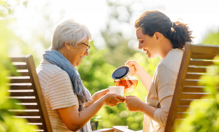 Happy young woman and her mother drinking tea in summer morning. Family sitting in the garden with cups and enjoying the conversation.の写真素材