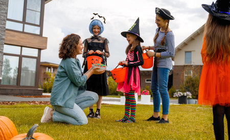 Happy people celebrating Halloween. Adult is treating with sweets children outdoors.の写真素材