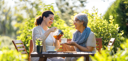 Happy young woman and her mother drinking tea in summer morning. Family sitting in the garden with cups and enjoying the conversation.の写真素材