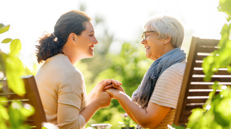 Happy young woman and her mother relaxing in summer morning. Family sitting in the garden and enjoying the conversation.の写真素材