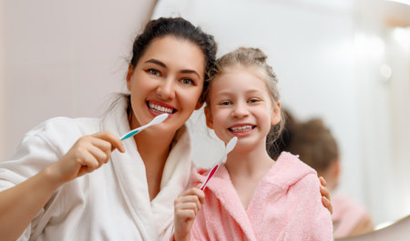 Happy family! Mother and daughter child girl are brushing teeth toothbrushes in the bathroom.の写真素材
