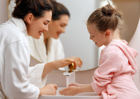 Cute little girl and her mother are washing hands under running water.の写真素材