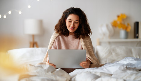 Happy casual beautiful woman wearing warm clothes is using laptop at home.の写真素材