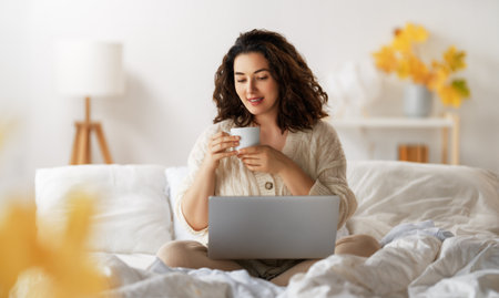 Happy casual beautiful woman wearing warm clothes is using laptop and drinking hot tea at home.の写真素材