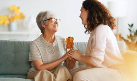 Happy adult woman and her senior mother with autumn leaves indoors.の写真素材