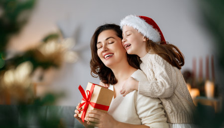 Merry Christmas and Happy Holidays. Cheerful mom and her cute daughter girl exchanging gifts. Parent and little child having fun near tree indoors.の写真素材