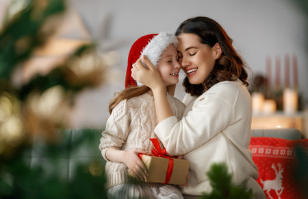 Merry Christmas and Happy Holidays. Cheerful mom and her cute daughter girl exchanging gifts. Parent and little child having fun near tree indoors.の写真素材