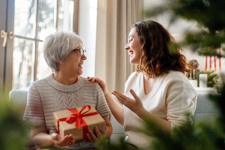 Merry Christmas and Happy Holidays! Senior mom and her adult daughter exchanging gifts. Having fun near tree indoors.の写真素材