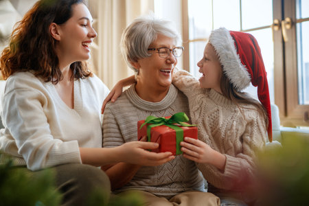 Merry Christmas and Happy Holidays. Cheerful kid presenting gifts to mom and granny. Parents and little child having fun near tree indoors. Loving family with presents in room.の写真素材