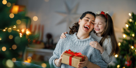Merry Christmas and Happy Holidays. Cheerful mom and her cute daughter girl exchanging gifts. Parent and little child having fun near tree indoors. Loving family with presents in room.の写真素材