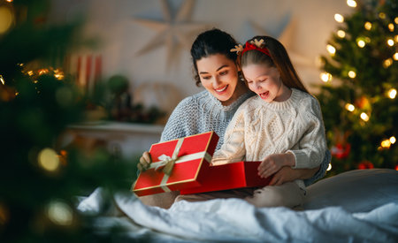 Merry Christmas and Happy Holidays. Cheerful mom and her cute daughter girl exchanging gifts. Parent and little child having fun near tree indoors. Loving family with presents in room.の写真素材