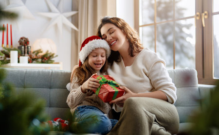 Merry Christmas and Happy Holidays. Cheerful mom and her cute daughter girl exchanging gifts. Parent and little child having fun near tree indoors.の写真素材