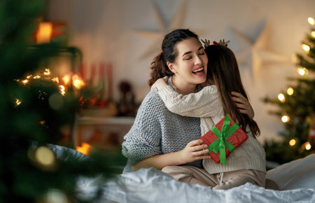 Merry Christmas and Happy Holidays. Cheerful mom and her cute daughter girl exchanging gifts. Parent and little child having fun near tree indoors. Loving family with presents in room.の写真素材