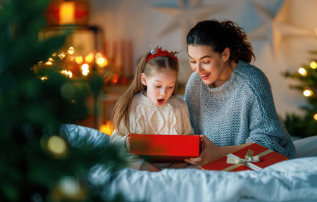 Merry Christmas and Happy Holidays. Cheerful mom and her cute daughter girl exchanging gifts. Parent and little child having fun near tree indoors. Loving family with presents in room.の写真素材