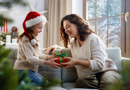 Merry Christmas and Happy Holidays. Cheerful mom and her cute daughter girl exchanging gifts. Parent and little child having fun near tree indoors.の写真素材