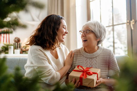 Merry Christmas and Happy Holidays! Senior mom and her adult daughter exchanging gifts. Having fun near tree indoors.の写真素材