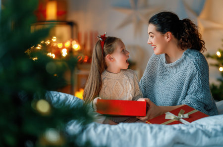 Merry Christmas and Happy Holidays. Cheerful mom and her cute daughter girl exchanging gifts. Parent and little child having fun near tree indoors. Loving family with presents in room.の写真素材
