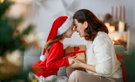 Merry Christmas and Happy Holidays. Cheerful mom and her cute daughter girl exchanging gifts. Parent and little child having fun near tree indoors.の写真素材