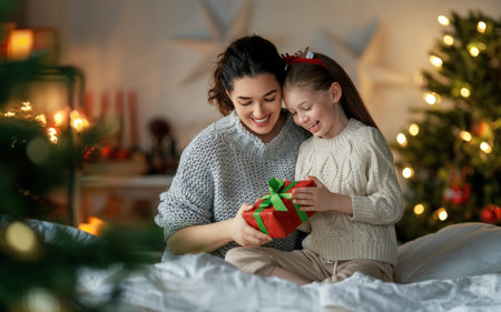 Merry Christmas and Happy Holidays. Cheerful mom and her cute daughter girl exchanging gifts. Parent and little child having fun near tree indoors. Loving family with presents in room.の写真素材