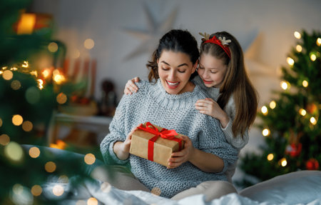 Merry Christmas and Happy Holidays. Cheerful mom and her cute daughter girl exchanging gifts. Parent and little child having fun near tree indoors. Loving family with presents in room.の写真素材